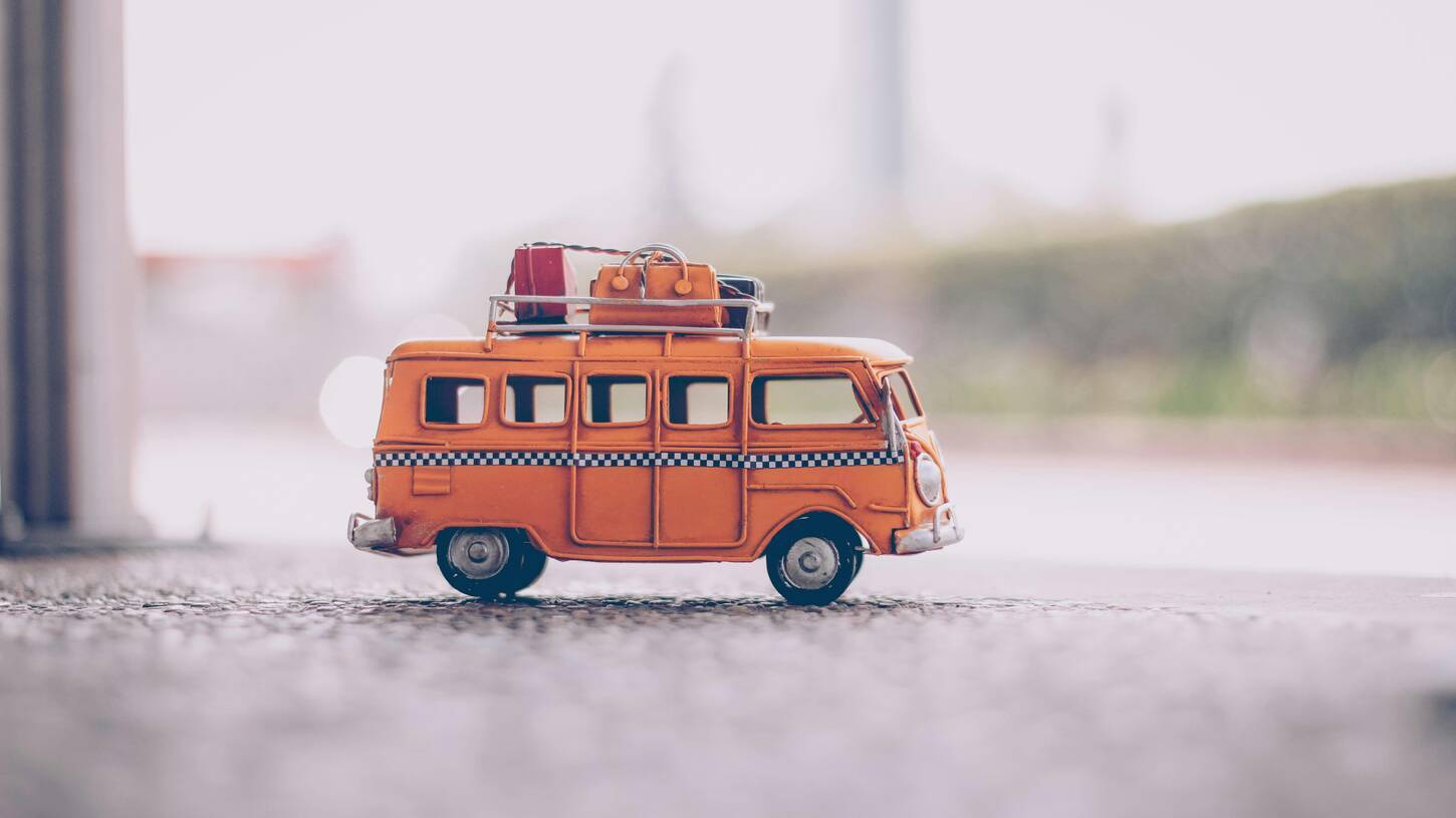 Een oranje speelgoed-bus met bagage op het dak.